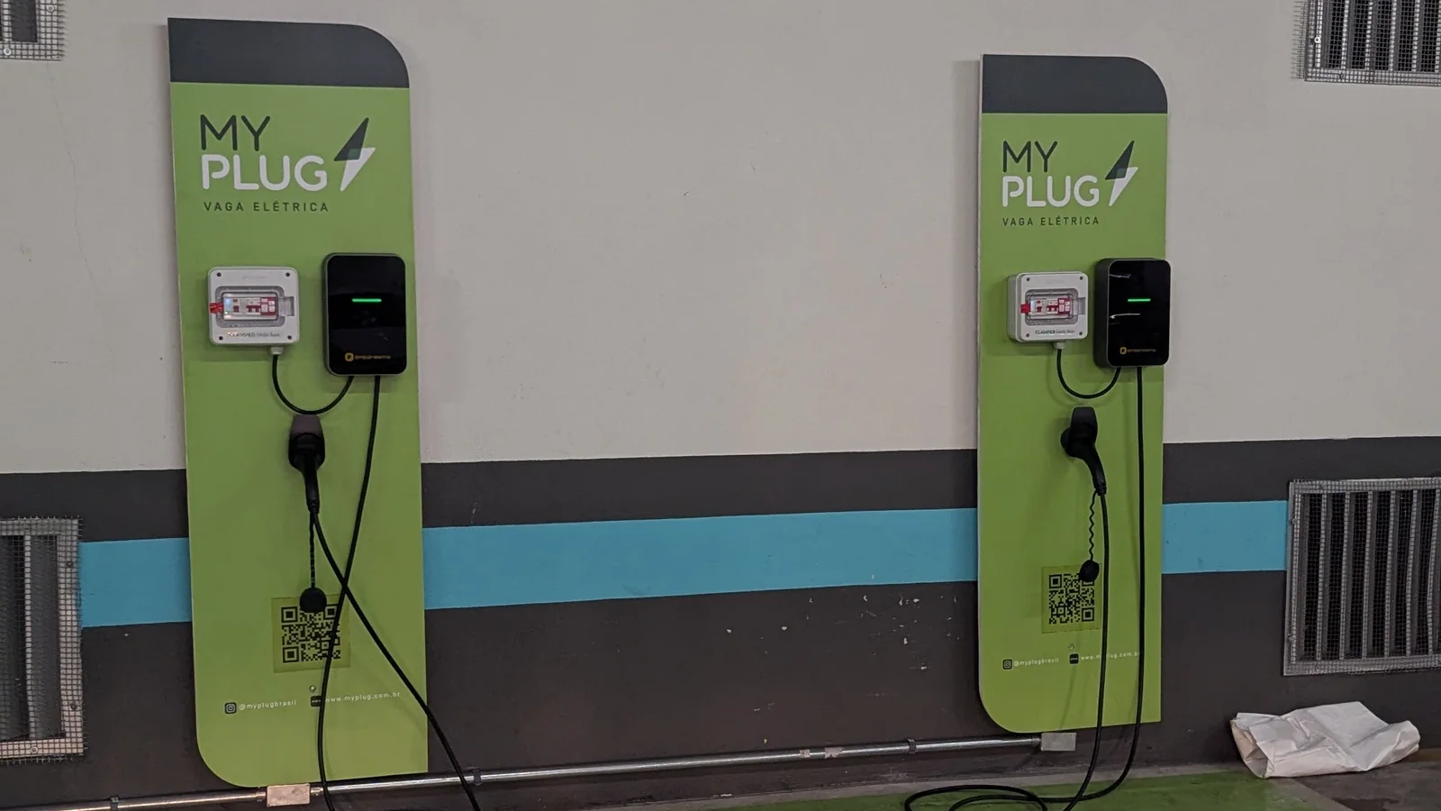 Duas vagas de estacionamento equipadas: cada painel traz um medidor, um carregador âmbar-e e o adesivo de QR Code que o motorista escaneia para pagar