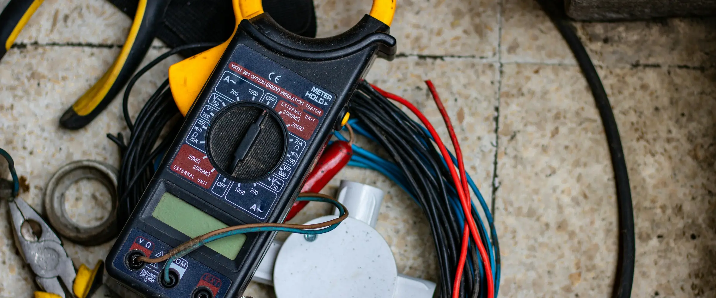 Alicate amperímetro, alicate e fios elétricos sobre o piso