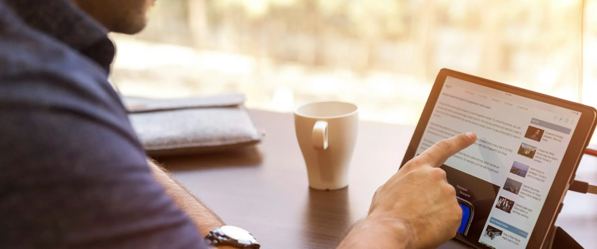 Pessoa lendo num tablet, com uma xícara de café sobre a mesa