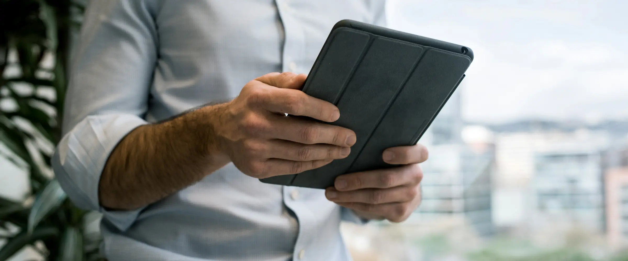 Pessoa segurando um tablet diante de uma janela com vista da cidade